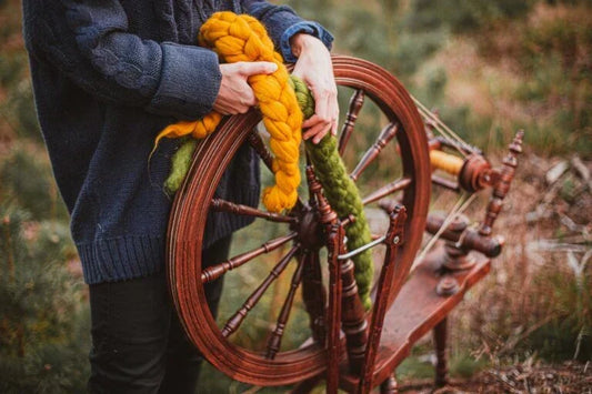 Person mit Spinnrad im Freien hält Kammzüge aus bunter Wolle, ideal für den Einstieg ins Spinnen mit dem Spinnrad
