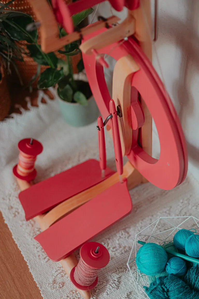Detailansicht des Kromski Fantasia Spinnrads in Coral Pink mit zwei vollen Spulen auf hellem Teppichboden.