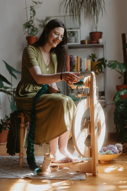 Spinnende Frau mit dem naturfarbenen Kromski Fantasia Spinnrad im gemütlichen Wohnzimmer mit Pflanzen.